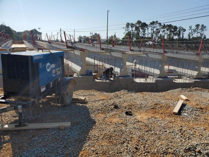 A crew member welding girders and bearing plates together to construct the new bridge over I-20 along Broad River Road. When combined, girders and bearing plates form sturdy, load-bearing structures.